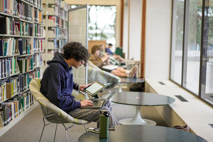 A student sitting at a table in the library studying on a laptop. 
