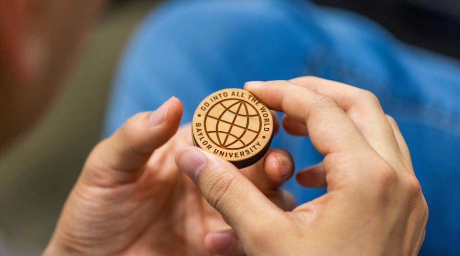 Baylor student holds coin reading: Go into all the world - Baylor University